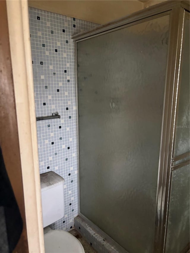 bathroom featuring toilet, tile walls, and a shower stall