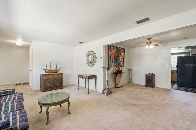 carpeted living area with ceiling fan, baseboards, visible vents, and a textured ceiling