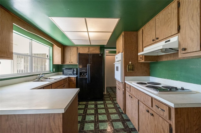 kitchen with black appliances, under cabinet range hood, a sink, dark floors, and light countertops