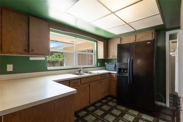 kitchen featuring black fridge with ice dispenser, light countertops, dark floors, and a sink