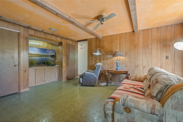 living room with tile patterned floors, beamed ceiling, wooden walls, and a ceiling fan