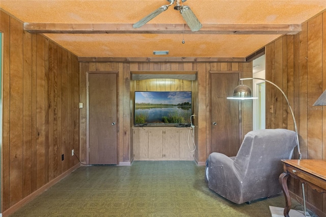 living area with beamed ceiling, baseboards, wooden walls, and a ceiling fan