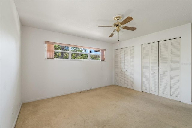 unfurnished bedroom featuring two closets, ceiling fan, and carpet