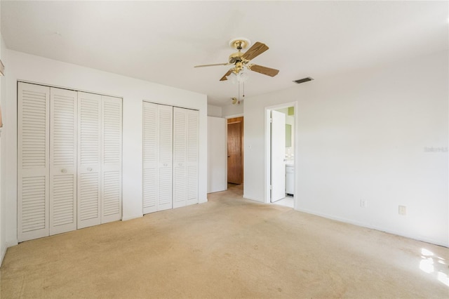 unfurnished bedroom featuring visible vents, connected bathroom, two closets, light carpet, and a ceiling fan