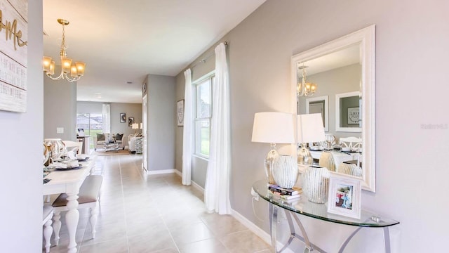 hallway with tile patterned flooring, baseboards, and an inviting chandelier