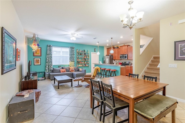 dining space with light tile patterned flooring, stairway, ceiling fan with notable chandelier, and baseboards