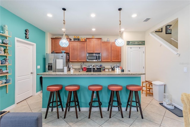 kitchen with visible vents, brown cabinets, a breakfast bar, a center island with sink, and stainless steel appliances