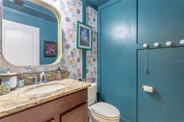 bathroom featuring toilet, wallpapered walls, and vanity