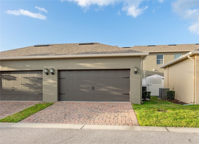 exterior space with a front yard, roof with shingles, stucco siding, a garage, and central air condition unit