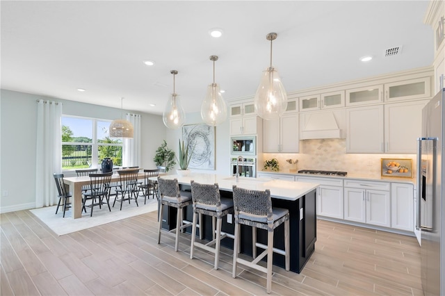 kitchen featuring visible vents, premium range hood, stainless steel appliances, light countertops, and tasteful backsplash