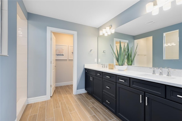 full bathroom featuring double vanity, baseboards, wood finish floors, and a sink