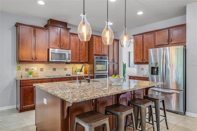 kitchen featuring a center island with sink, a sink, backsplash, appliances with stainless steel finishes, and light stone countertops