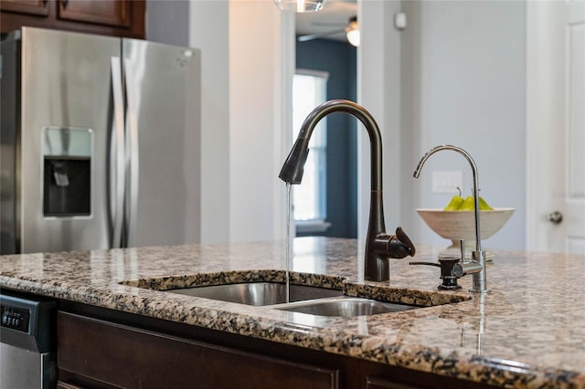 kitchen with dark brown cabinets, light stone counters, appliances with stainless steel finishes, and a sink