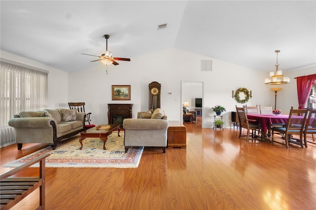 living area featuring a glass covered fireplace, lofted ceiling, visible vents, and light wood-type flooring