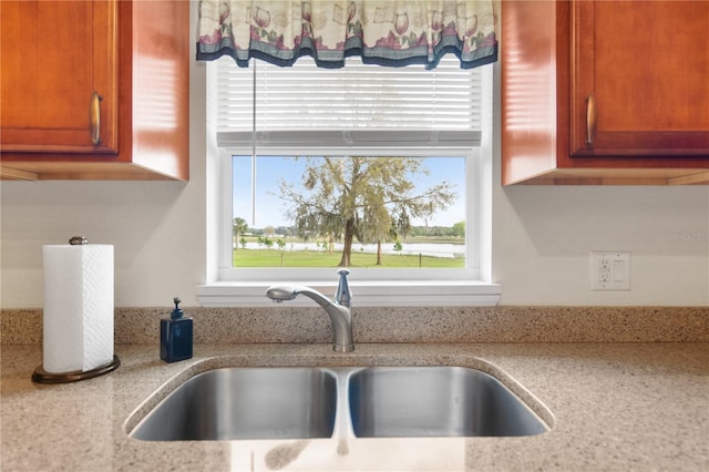 kitchen featuring brown cabinetry, light stone countertops, and a sink