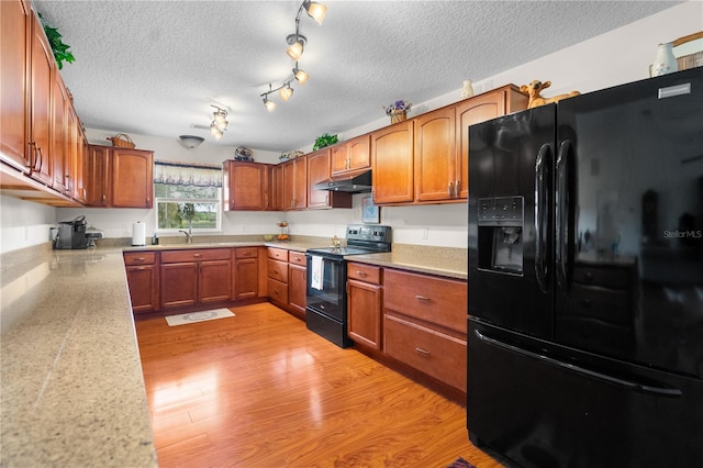 kitchen with light wood finished floors, black appliances, under cabinet range hood, brown cabinetry, and light countertops