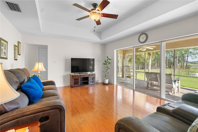 living area with visible vents, a ceiling fan, a tray ceiling, wood finished floors, and baseboards