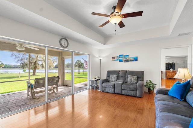 living room with a healthy amount of sunlight, a tray ceiling, and wood finished floors