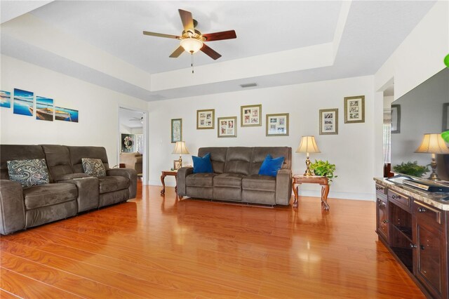 living room featuring a raised ceiling, a ceiling fan, light wood-type flooring, and visible vents