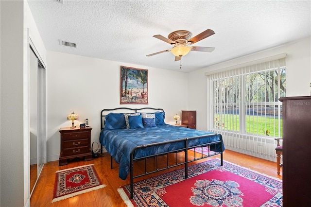 bedroom with visible vents, ceiling fan, wood finished floors, a closet, and a textured ceiling