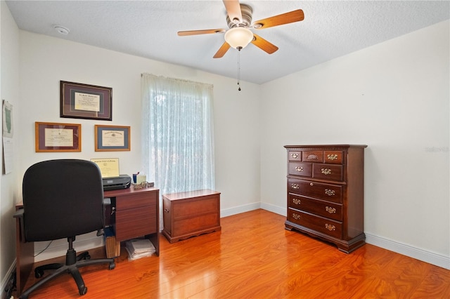 home office with a textured ceiling, baseboards, light wood-type flooring, and ceiling fan