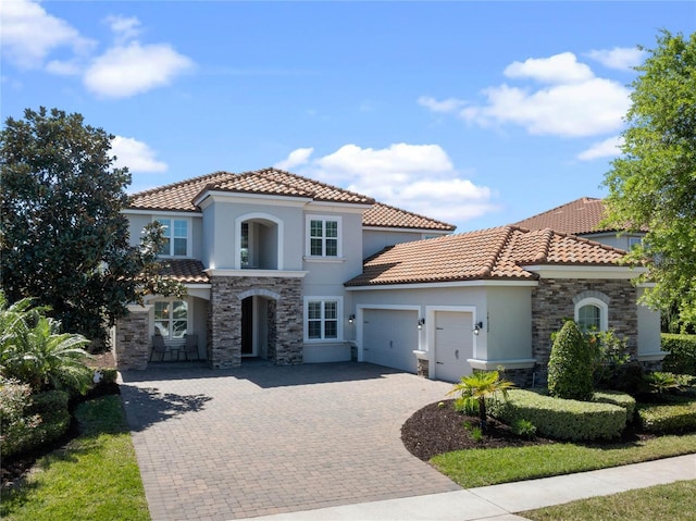 mediterranean / spanish home with decorative driveway, an attached garage, stone siding, and stucco siding