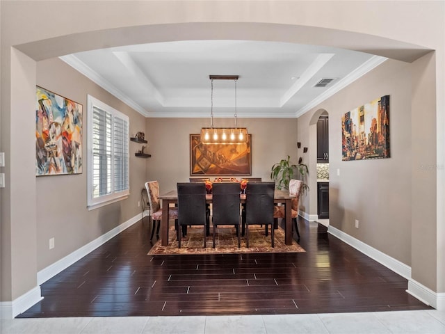 dining space with a tray ceiling, wood finished floors, visible vents, and baseboards