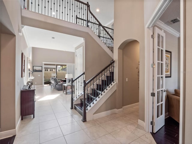 entrance foyer featuring arched walkways, visible vents, baseboards, and a towering ceiling