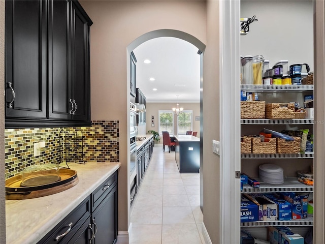 kitchen with decorative backsplash, dark cabinetry, light tile patterned floors, and arched walkways