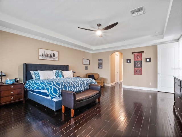 bedroom with dark wood-style floors, visible vents, baseboards, a tray ceiling, and arched walkways