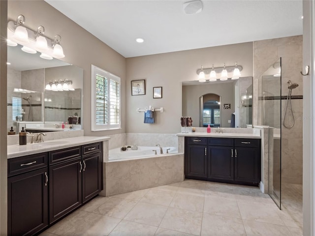 full bath featuring tile patterned flooring, walk in shower, a garden tub, two vanities, and a sink