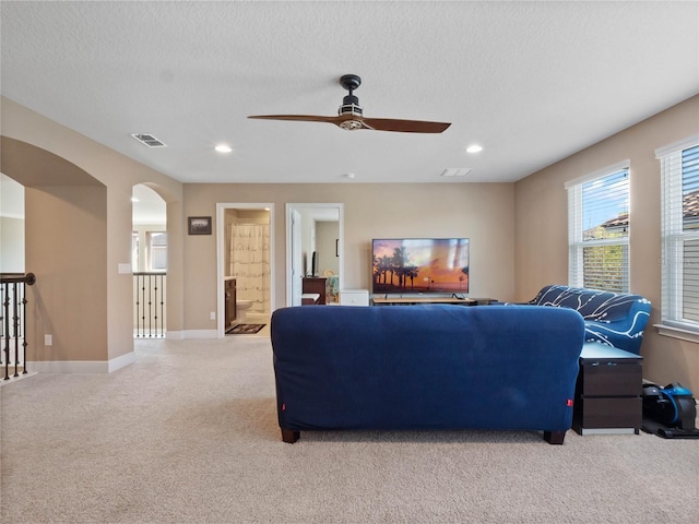 living room with visible vents, arched walkways, light colored carpet, and a textured ceiling