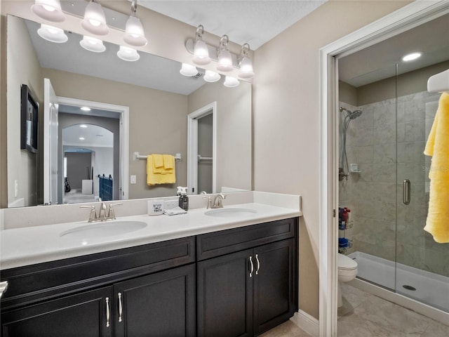 full bathroom with a sink, toilet, double vanity, and a shower stall