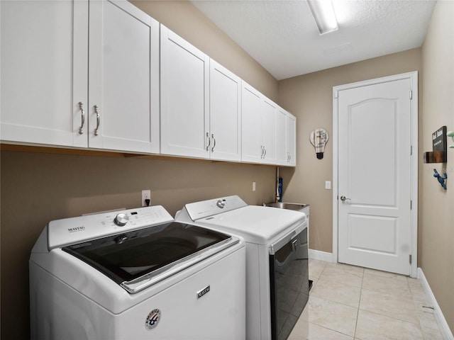 laundry area featuring cabinet space, light tile patterned floors, washing machine and dryer, and baseboards