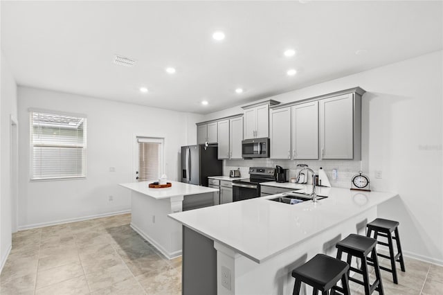 kitchen featuring a breakfast bar, gray cabinets, stainless steel appliances, and a sink