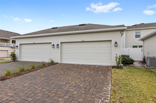 garage with cooling unit, decorative driveway, and fence