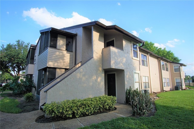 view of front of property with a front yard, central AC, and stucco siding