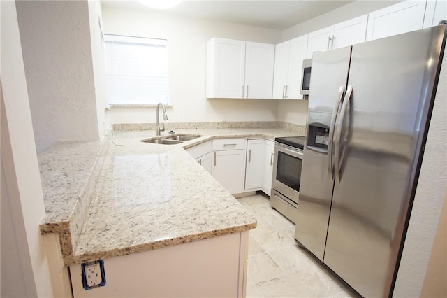 kitchen with a sink, light stone counters, appliances with stainless steel finishes, white cabinets, and a textured wall