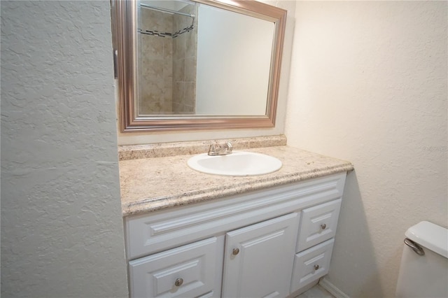 bathroom with toilet, vanity, and a textured wall