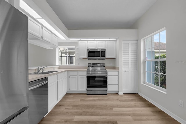 kitchen featuring light wood finished floors, a sink, stainless steel appliances, light countertops, and white cabinetry