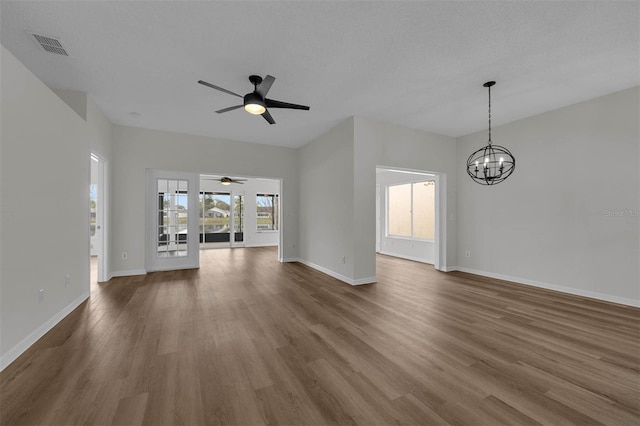 unfurnished living room with a wealth of natural light, baseboards, dark wood finished floors, and ceiling fan with notable chandelier