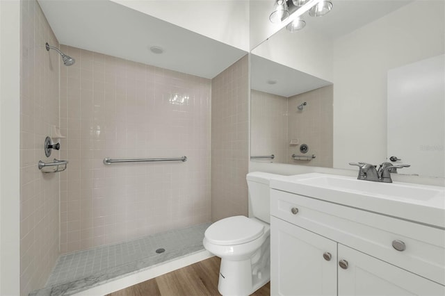 bathroom with vanity, toilet, wood finished floors, and tiled shower