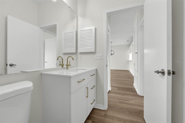 half bath featuring toilet, vanity, baseboards, and wood finished floors