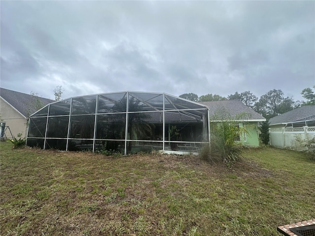 rear view of house with a lanai, a yard, and fence