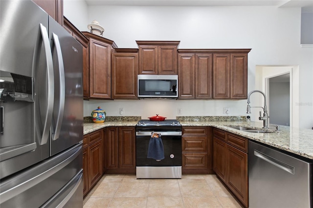 kitchen featuring light tile patterned floors, light stone countertops, appliances with stainless steel finishes, and a sink