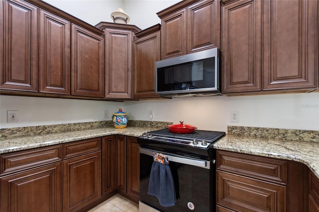 kitchen featuring light stone counters, built in desk, dark brown cabinets, and stainless steel appliances