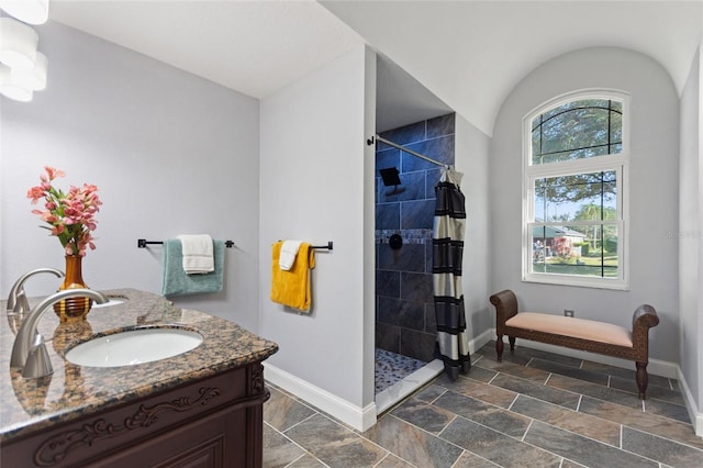 bathroom featuring vanity, baseboards, a tile shower, and stone finish flooring