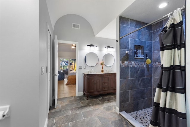 bathroom with visible vents, tiled shower, double vanity, lofted ceiling, and a sink