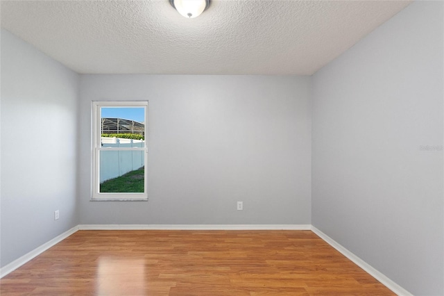 empty room featuring baseboards, light wood-style floors, and a textured ceiling