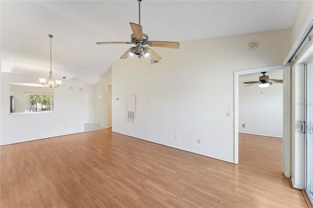 spare room with lofted ceiling, ceiling fan with notable chandelier, light wood-type flooring, and a textured ceiling